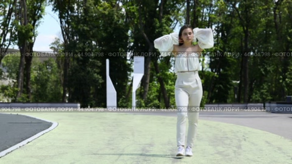 Young beautiful brunette girl in a beige dress walks in a summer city park. Стоковое видео, видеограф Андрей Аркуша / Фотобанк Лори