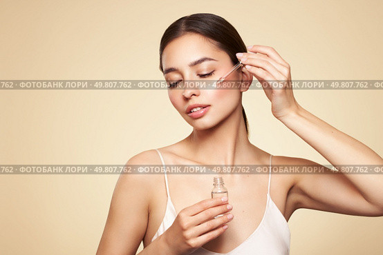 Young beautiful woman applying face serum with pipette. Cosmetic procedures for facial skin care. Стоковое фото, агентство Ingram Publishing / Фотобанк Лори