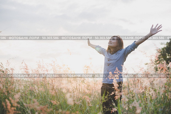 Young beautiful woman standing stretch her arms in the air on the grass field. Woman enjoy with nature during sunset. Стоковое фото, агентство Ingram Publishing / Фотобанк Лори