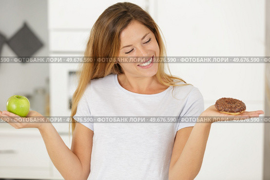 young blond woman is holding an apple and a donut. Стоковое фото, агентство Ingram Publishing / Фотобанк Лори