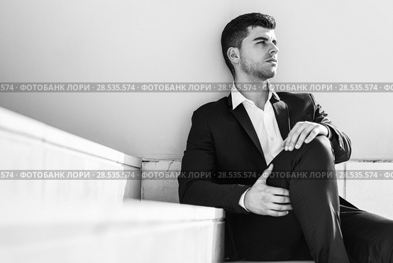 Young businessman near a modern office building wearing black suit and white shirt sitting on the floor. Man with blue eyes in urban background. Стоковое фото, фотограф Javier Sánchez Mingorance / Ingram Publishing / Фотобанк Лори