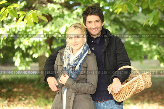 young couple behind trees in autumn, man holding a wickerwork basket. Стоковое фото, агентство Ingram Publishing / Фотобанк Лори