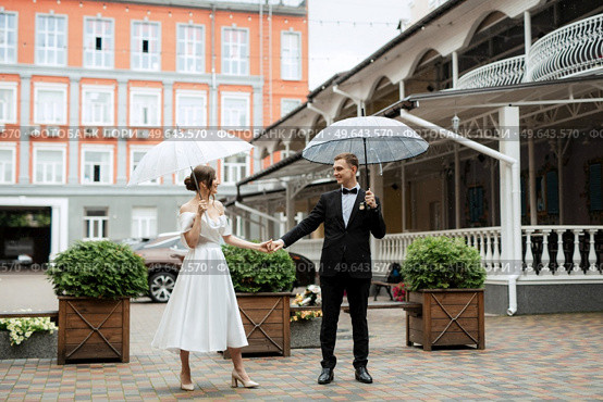 young couple bride and groom in a white short dress walking in the rain. Стоковое фото, агентство Ingram Publishing / Фотобанк Лори
