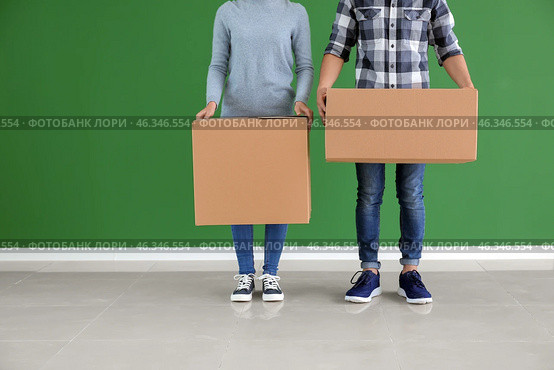 Young couple with boxes near color wall indoors. Moving into new house. Стоковое фото, фотограф Pixel_shot / Фотобанк Лори