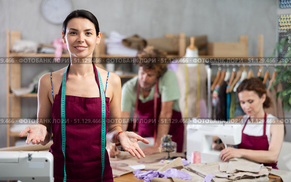 Young female dressmaker inviting clients while others sew and draw. Стоковое фото, фотограф Яков Филимонов / Фотобанк Лори