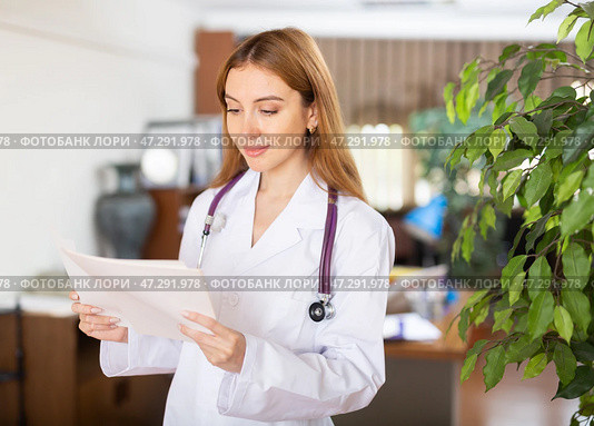 Young female therapist is studying important documents while standing in the office. Стоковое фото, фотограф Яков Филимонов / Фотобанк Лори