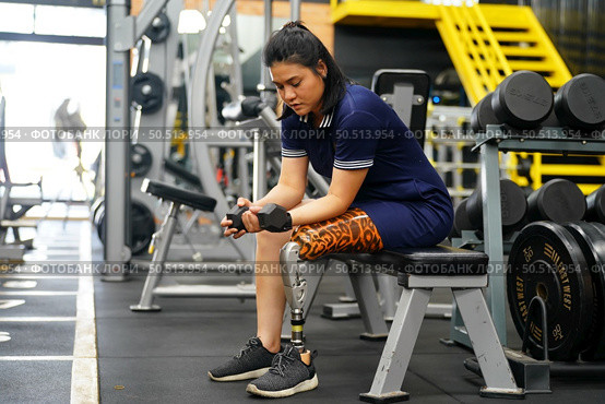 Young female with one prosthetic leg warms up by lifting light weights. Concept of living a woman’s life with a prosthetic limb. Стоковое фото, агентство Ingram Publishing / Фотобанк Лори