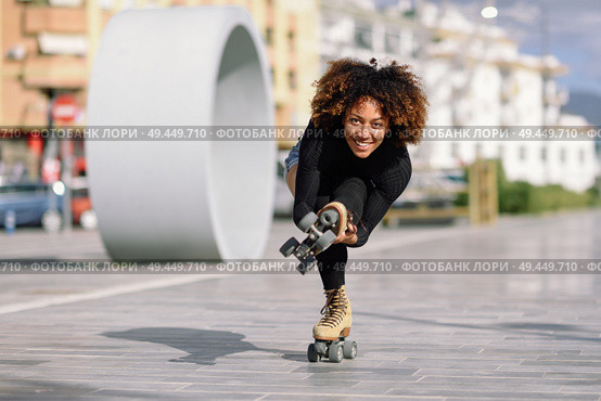Young fit black woman on roller skates riding outdoors on urban street. Smiling girl with afro hairstyle rollerblading on sunny day. Black woman on roller skates riding outdoors on urban street. Стоковое фото, агентство Ingram Publishing / Фотобанк Лори