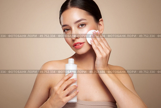 Young girl holds cotton pad while cleansing face with cosmetic milk. Skin care removal of makeup cleansing. Basic facial skin care. Стоковое фото, агентство Ingram Publishing / Фотобанк Лори