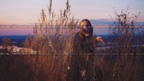 Young girl is dancing in the grass against the background of the sunset. Стоковое видео, видеограф Strunov David / Фотобанк Лори