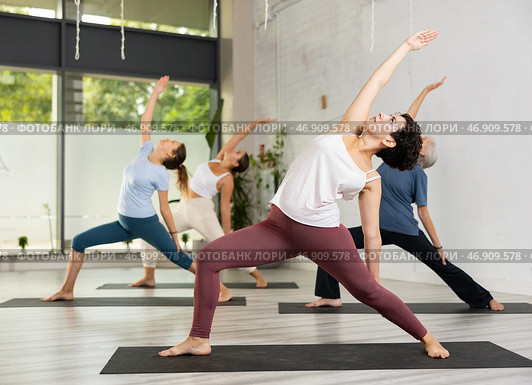 Young Latin female practicing Revolved Side Angle Pose Parivrtta Parsvakonasana, balancing posture of Hatha yoga during group workout in studio. Стоковое фото, фотограф Яков Филимонов / Фотобанк Лори