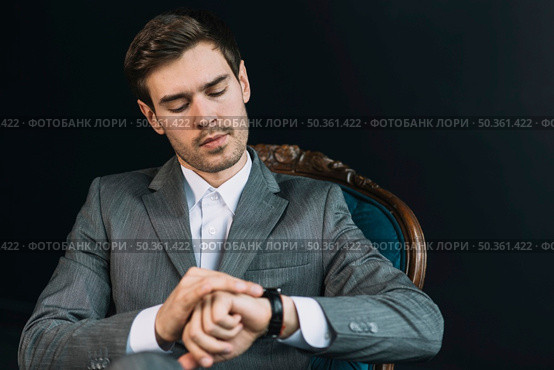 young man checking time his watch against black background. Стоковое фото, агентство Ingram Publishing / Фотобанк Лори