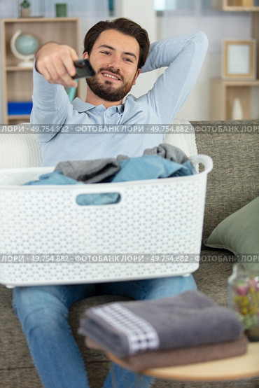 young man prefers to watch tv than doing laundry. Стоковое фото, агентство Ingram Publishing / Фотобанк Лори