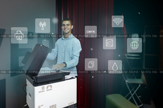 Young man using a multifunction printer in an office environment, showcasing modern technology and digital integration. Стоковое фото, фотограф Сергей Толмачёв / Фотобанк Лори