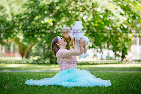 Young mother with child in park sitting on grass on a summer day. Lifts the child into the air. The concept of right relationships. Стоковое фото, фотограф Иван Карпов / Фотобанк Лори