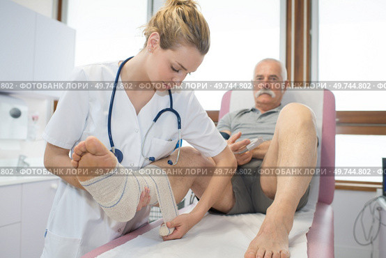 young nurse bandaging mans foot in clinic. Стоковое фото, агентство Ingram Publishing / Фотобанк Лори