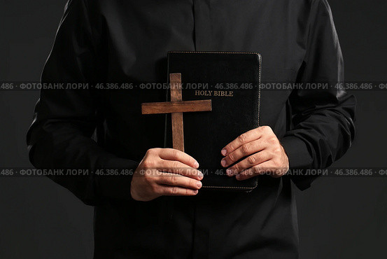 Young priest with Bible and cross on dark background. Стоковое фото, фотограф Pixel_shot / Фотобанк Лори
