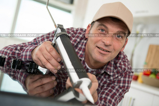 young repairman working at the kitchen with glue gun. Стоковое фото, агентство Ingram Publishing / Фотобанк Лори