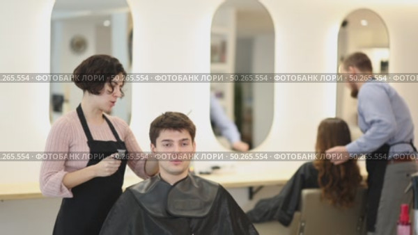 Young woman barbershop employee stands next to male client, discussing details of haircut. Стоковое видео, видеограф Яков Филимонов / Фотобанк Лори