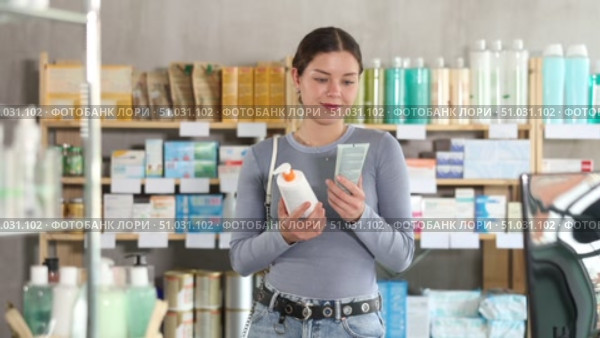 Young woman comparing two skincare products with interest at pharmacy, pump bottle and tube, exploring difference in texture, purpose or ingredients before making purchase. Стоковое видео, видеограф Яков Филимонов / Фотобанк Лори