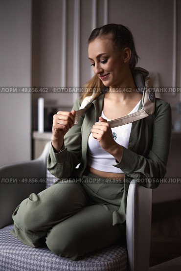 Young Woman Enjoys Relaxation With a Neck Massager in a Cozy Indoor Setting. Стоковое фото, фотограф Aleksandr Golubev / Фотобанк Лори