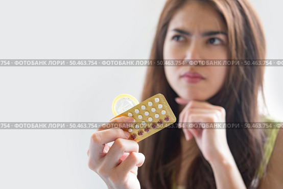 Young woman holding condom and contraceptive pills prevent pregnancy. Стоковое фото, агентство Ingram Publishing / Фотобанк Лори