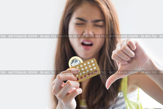 Young woman holding condom and contraceptive pills prevent pregnancy. Стоковое фото, агентство Ingram Publishing / Фотобанк Лори