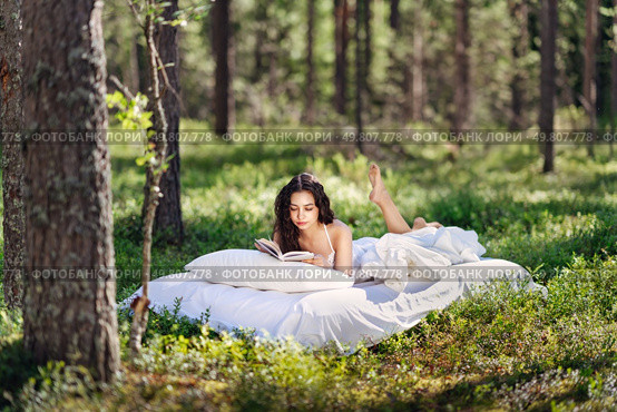 Young woman is reading a book in the forest lying on a mattress. The girl relaxing in nature. Стоковое фото, агентство Ingram Publishing / Фотобанк Лори