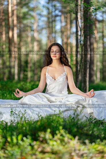 Young woman is resting on a mattress in the lotus position, in summer forest. Girl is sleeping in the woods. Стоковое фото, агентство Ingram Publishing / Фотобанк Лори
