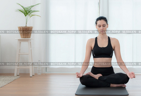 Young woman meditating in lotus pose on exercise mat at home, Yoga exercise concept. Стоковое фото, агентство Ingram Publishing / Фотобанк Лори