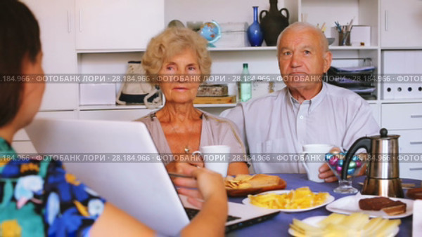 Young woman showing elderly couple something interesting on laptop over cup of tea. Стоковое видео, видеограф Яков Филимонов / Фотобанк Лори