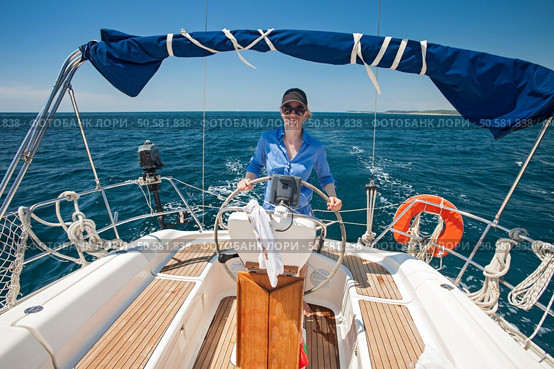 Young woman standing at the helm of a boat against a blue sky. Стоковое фото, агентство Ingram Publishing / Фотобанк Лори