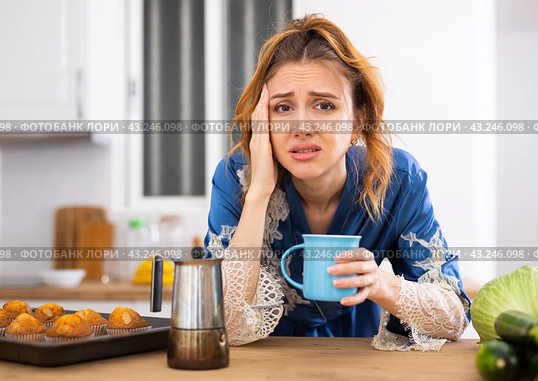 Young woman suffering from migraine, drinking coffee in home kitchen. Стоковое фото, фотограф Татьяна Яцевич / Фотобанк Лори