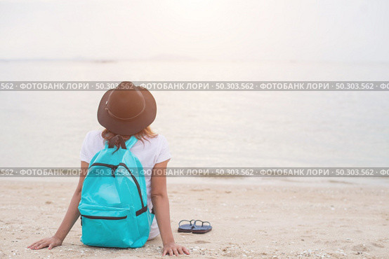 Young woman with backpack sitting on lonely beach and looking into distance. Стоковое фото, агентство Ingram Publishing / Фотобанк Лори