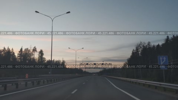 Загородная скоростная магистраль. Летний вечер, сумерки. Небо почти чистое светло-голубое. Асфальтовая дорога с двумя полосами в одну сторону с определением и ограждением. Машина двигается вперед, сохраняя при этом фары машин продовольственной безопасности. Стоковое видео, видеограф Andrew_Swarga / Фотобанк Лори