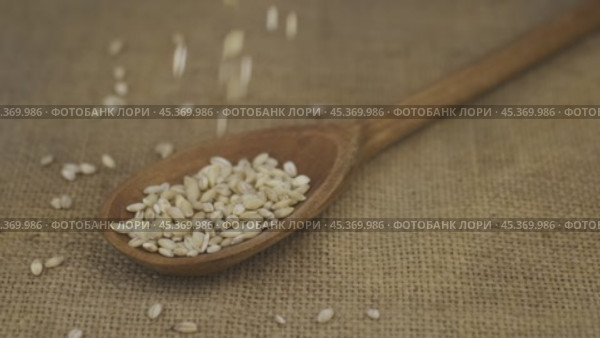 Замедленная съемка. Зерна перловой крупы сыплются в деревянную ложку, лежащую на мешковине. Горка зерна в ложке. Концепция изобилия продуктов. Стоковое видео, видеограф Александр Собко / Фотобанк Лори