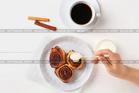 Женщина добавляет сливки на вкусные булочки с корицей на белом деревянном фоне. Стоковое фото, фотограф Pixel_shot / Фотобанк Лори