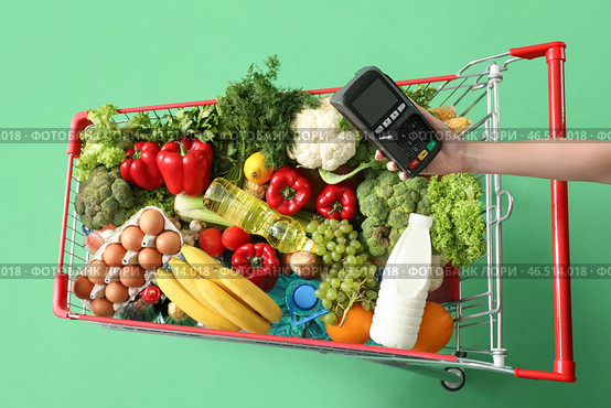 Женщина с платежным терминалом толкает тележку, полную продуктов, на зеленом фоне. Стоковое фото, фотограф Pixel_shot / Фотобанк Лори