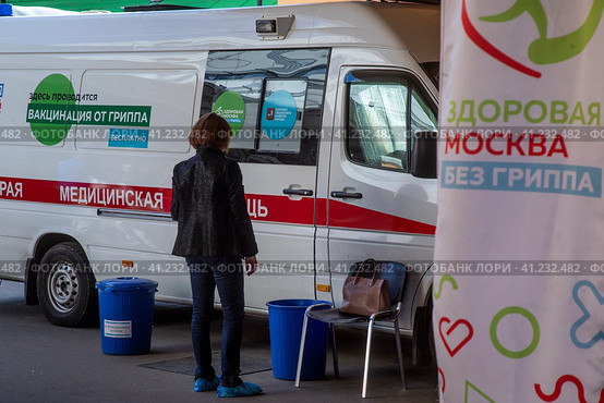 Женщина ждет своей очерди на вакцинацию у мобильного пункта бесплатной вакцинации от гриппа в специальном автомобиле скорой помощи в городе Москве, Россия (2023 год). Редакционное фото, фотограф Николай Винокуров / Фотобанк Лори