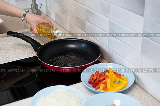 Женская рука наливает кукурузное масло из бутылки на разогретую сковородку, рядом нарезаны подготовленные овощи для жарки. Стоковое фото, фотограф Алиса Сокол / Фотобанк Лори