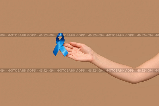 Женская рука с синей лентой на бежевом фоне. Концепция осведомленности о раке толстой кишки. Стоковое фото, фотограф Pixel_shot / Фотобанк Лори