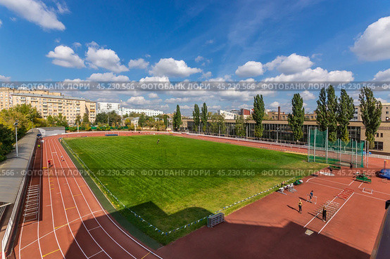 Znamensky Brothers stadium, Stromynka 4 - 03.09.2019: An athletic track showcases bright red lanes adjacent to a modern building, surrounded by green trees and a blue sky filled with fluffy clouds during a sunny day. Стоковое фото, фотограф Алексей Климкин / Фотобанк Лори